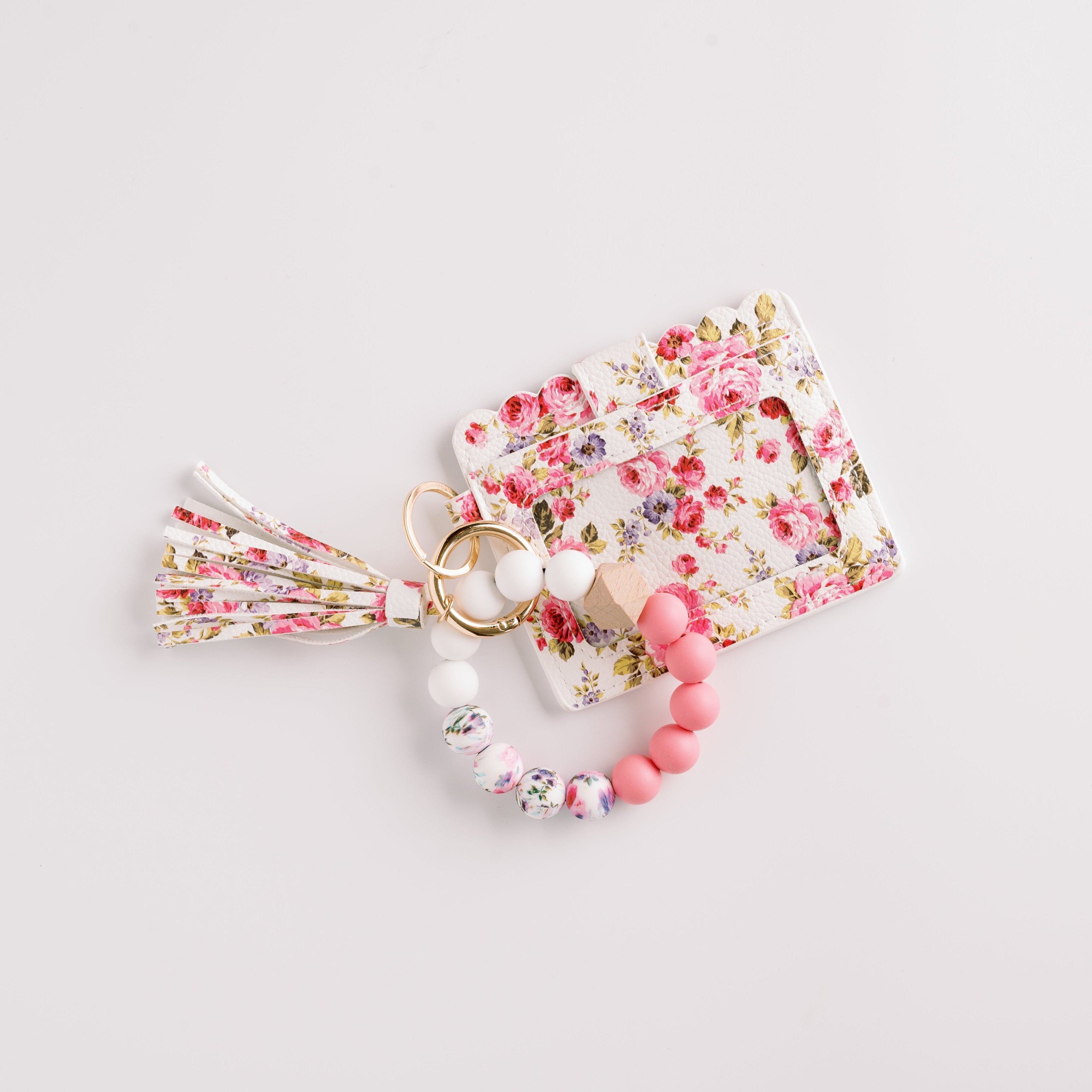 Floral cardholder with tassel keyring and beaded bracelet in pastel pink and white on white background.
