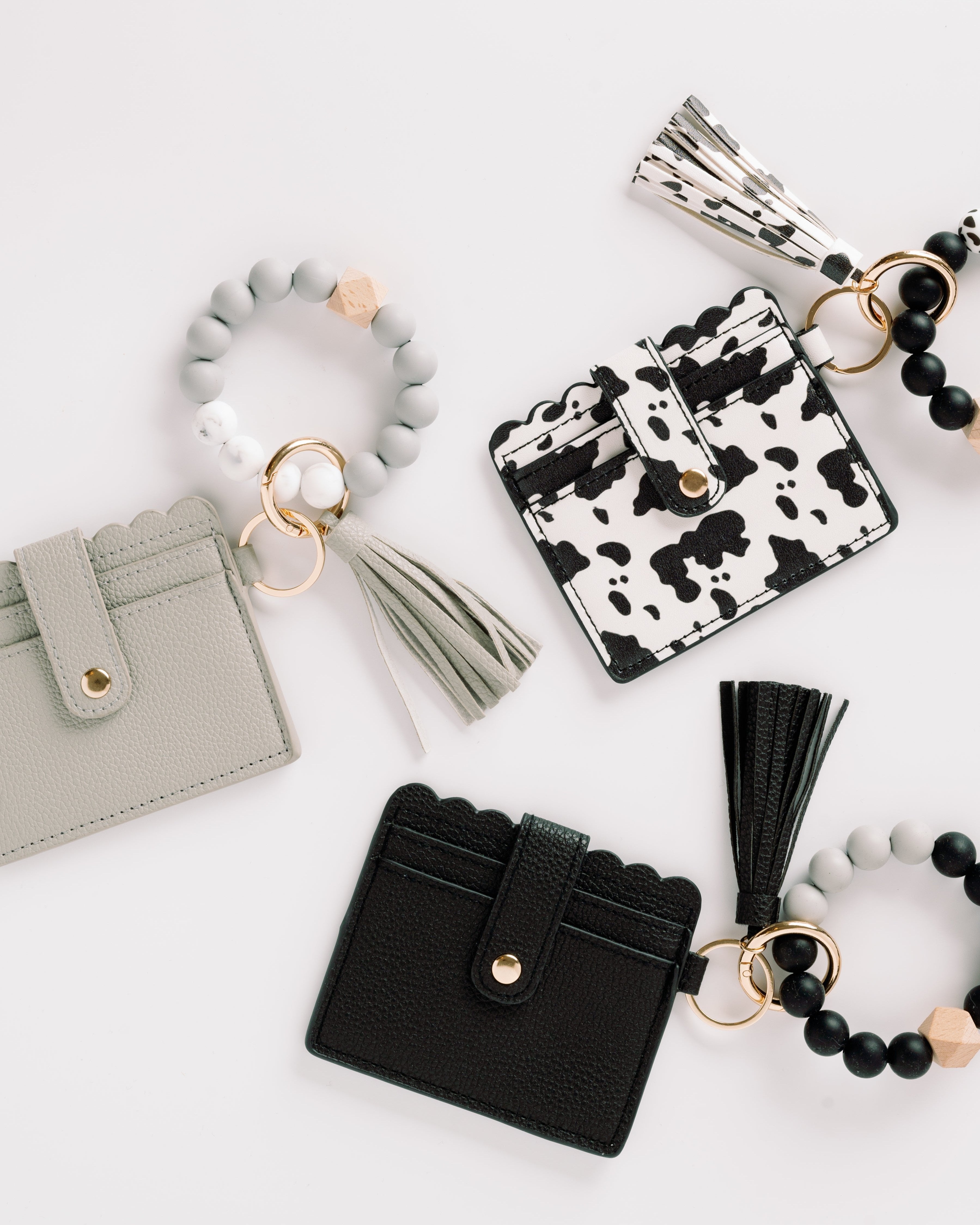 Stylish cardholders with tassels and beaded keychains in black, gray, and cow print.