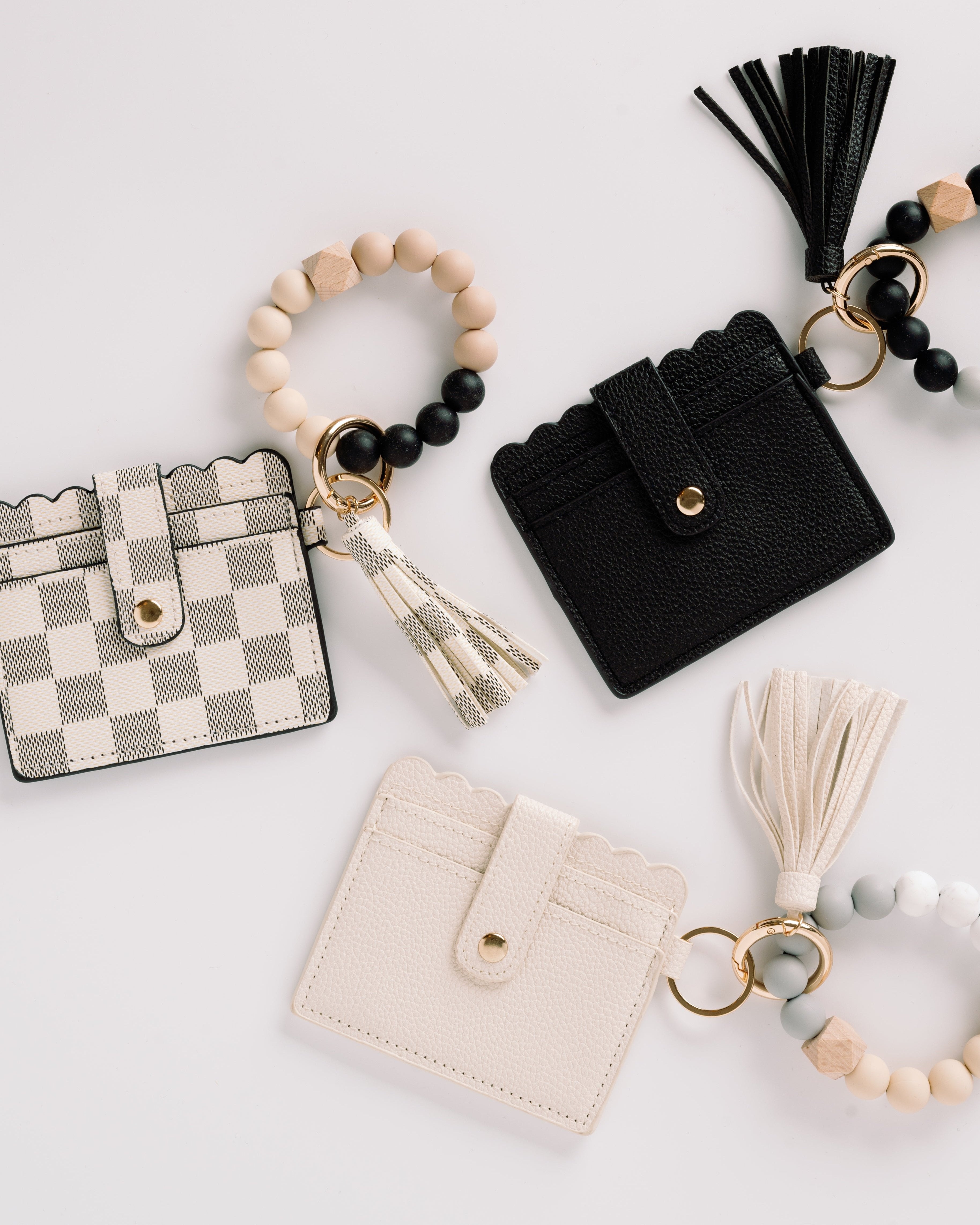 Scalloped cardholders in cream, black, and checkered patterns with tassels and beaded keyrings.