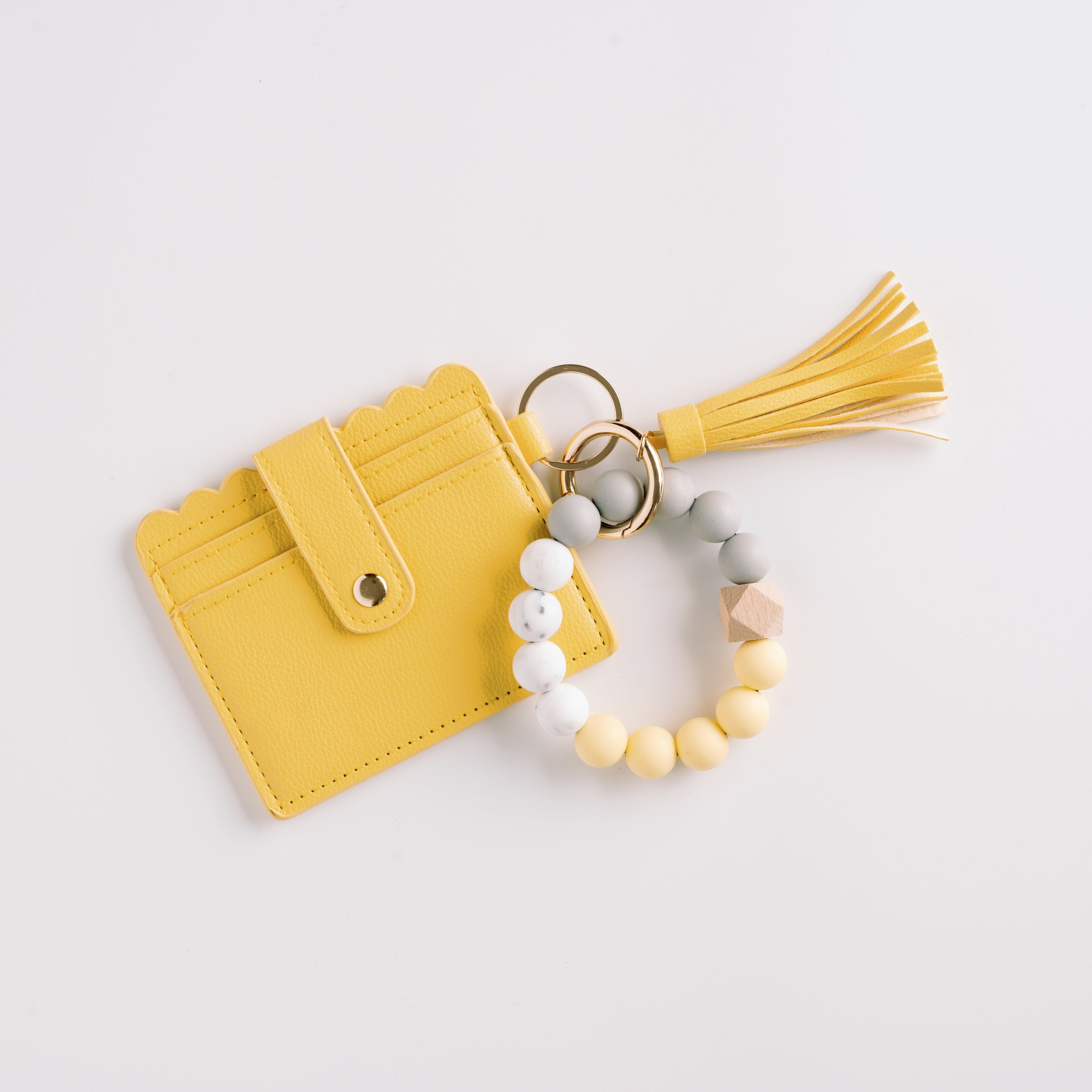 Yellow cardholder with scalloped edge, tassel, and bead bracelet in grey, yellow, and beige.