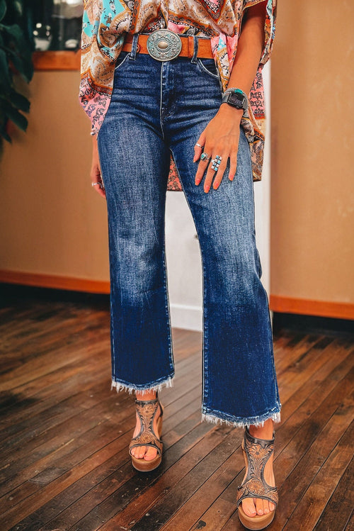 Woman wearing flared jeans, fringe hem, belt with silver buckle, patterned top, rings, and sandals.