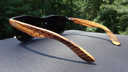 Black sunglasses with striped wooden arms on a dark fabric surface, green forest in background.