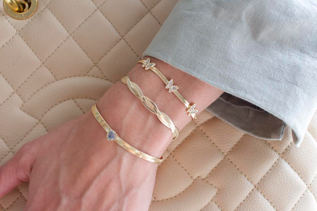 Wrist with gold bracelets on a quilted beige bag, wearing a light grey sleeve.