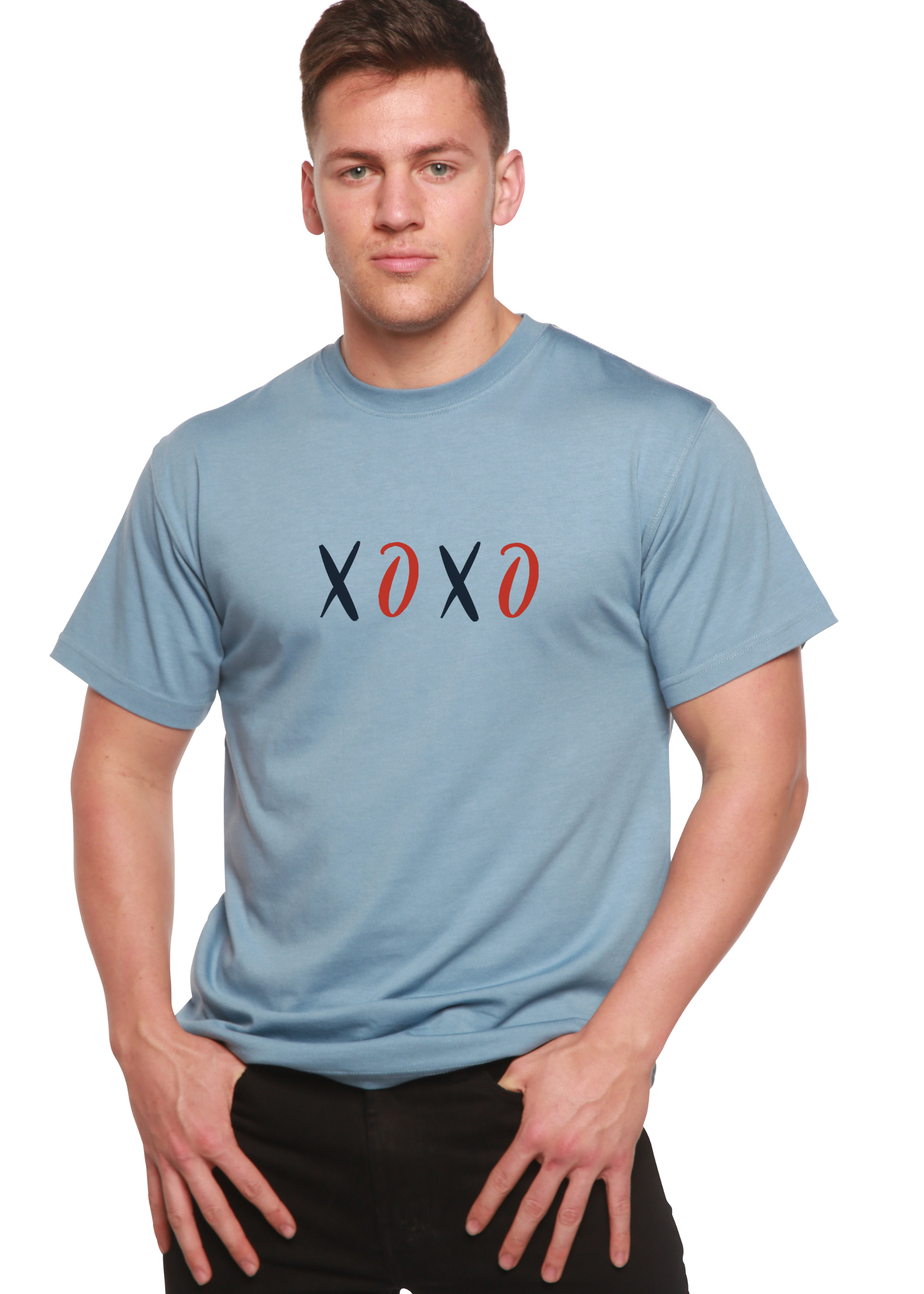 Man wearing a light blue T-shirt with "XOXO" in black and red letters, hands in pockets.