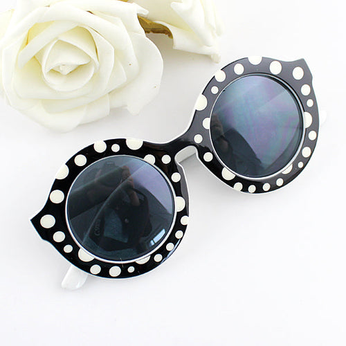 Black sunglasses with white polka dots on the frame, placed next to white roses.