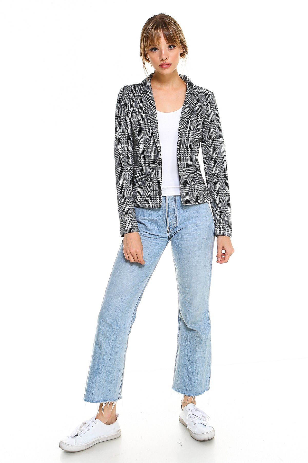 Woman in plaid blazer, white top, light jeans, and white sneakers, standing against a white background.