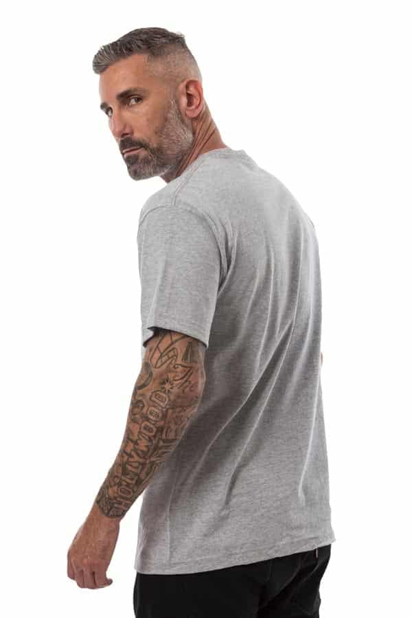 Man with short hair, beard, tattooed arm, in a gray T-shirt and black pants, looking over shoulder.
