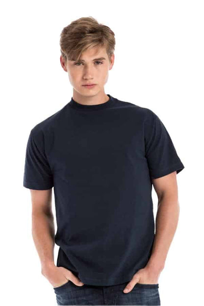 Young man in a plain dark blue t-shirt and jeans, standing with hands in pockets.