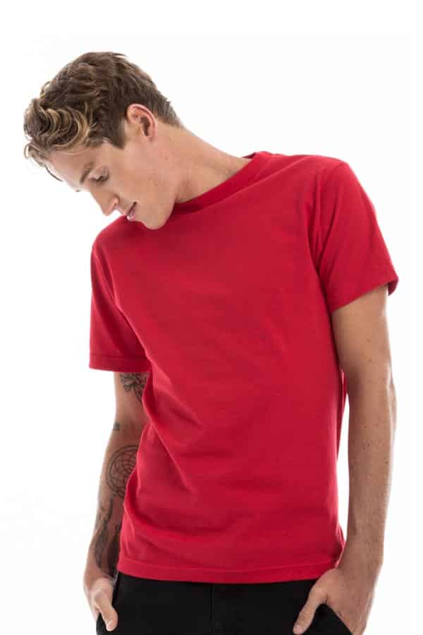 Man in a red T-shirt with tattoos, looking down, against a plain white background.