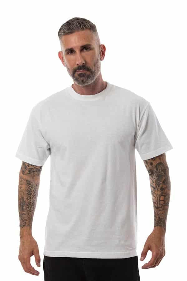 Man with a beard wearing a plain white T-shirt and black pants, with tattooed arms, on a white background.