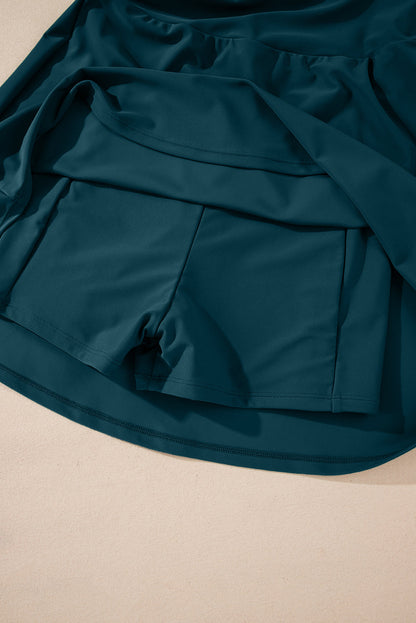 Dark teal shorts with flowing fabric overlay, displayed on a light surface.