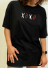 Curly-haired woman wearing a black "XOXO" t-shirt with a brown watch and light ring.