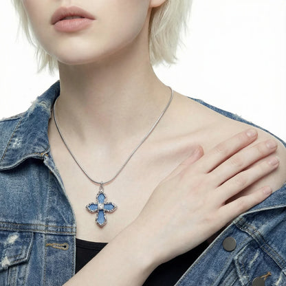 Person wearing a denim jacket and a silver necklace with a blue, cross-shaped pendant.