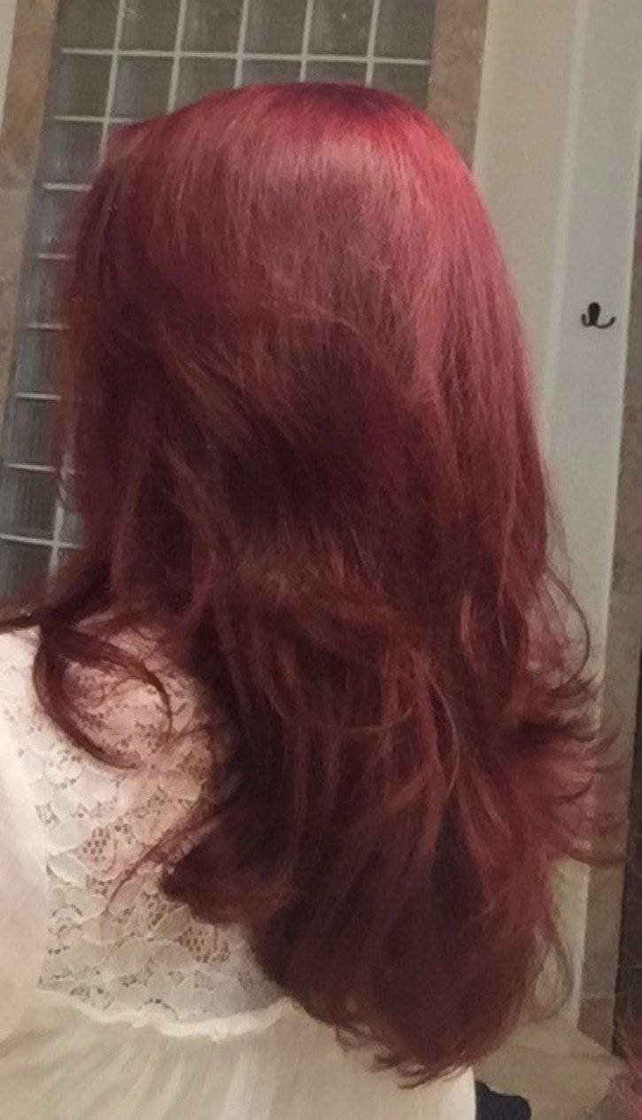 Person with long, wavy red hair, wearing a white lace top, in front of a tiled wall.