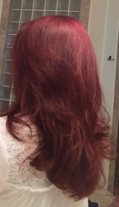 Person with long, wavy red hair, wearing a white lace top, in front of a tiled wall.