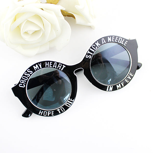 Black sunglasses with round lenses and white text, beside white roses.