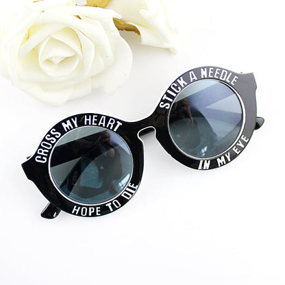 Black sunglasses with round lenses and white text, beside white roses.