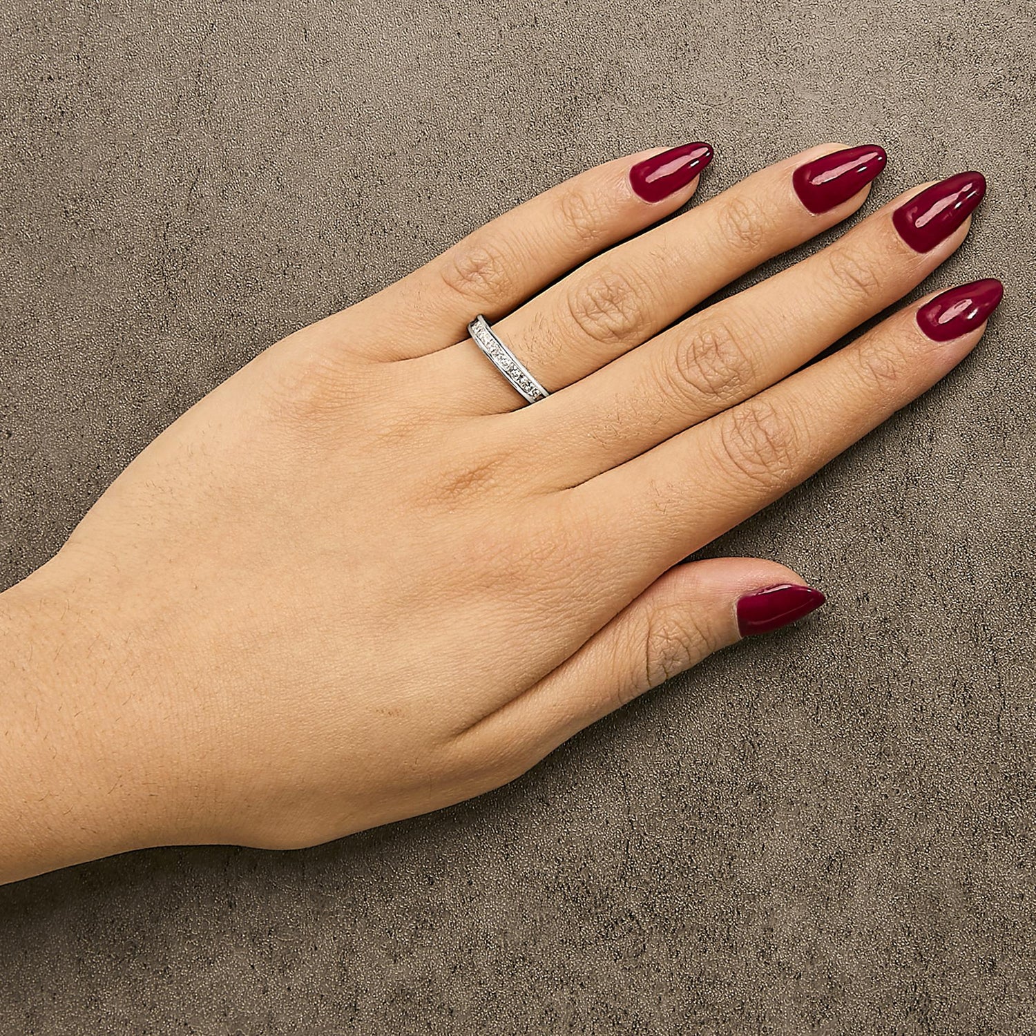 Hand with maroon nails and a silver ring on a textured gray surface.