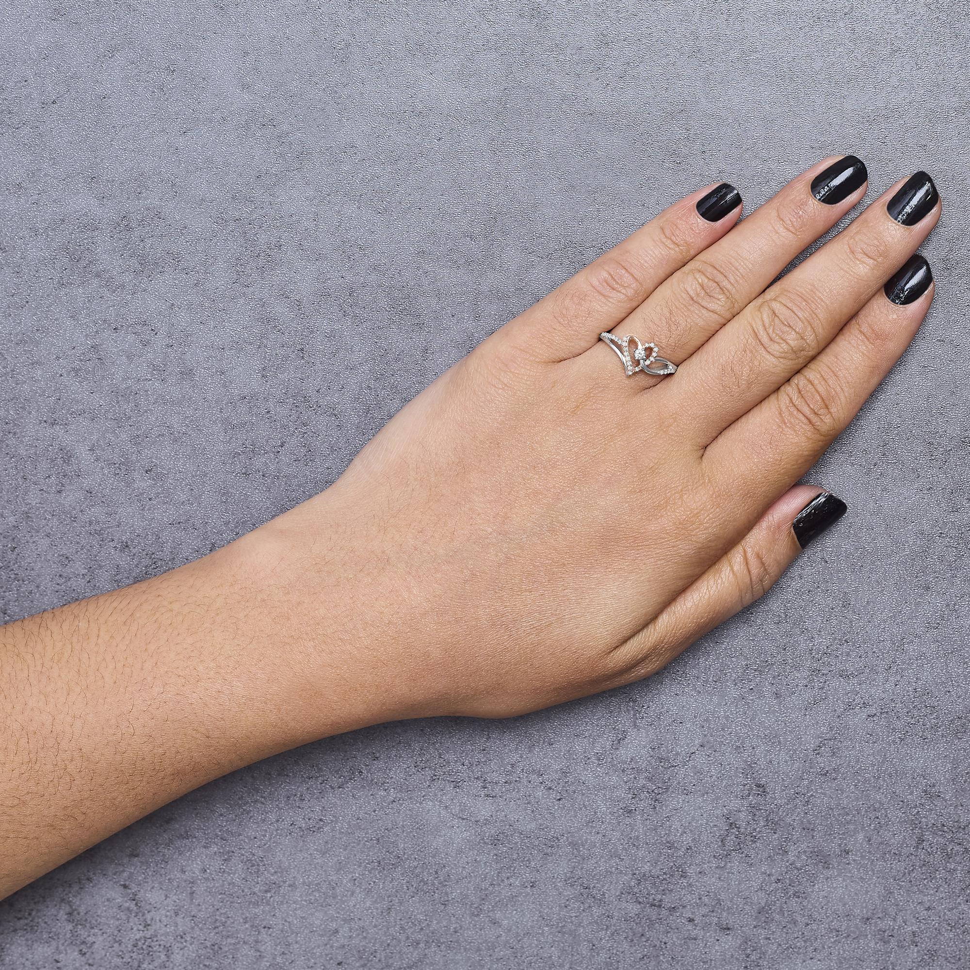 Hand with black nails wearing a silver ring on a gray textured surface.