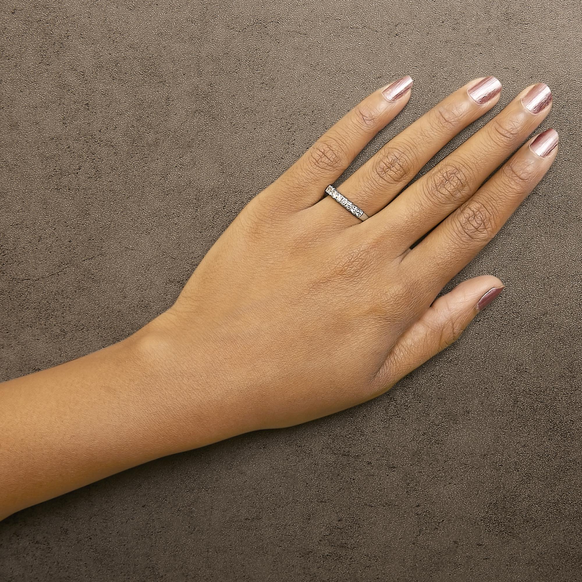 Hand with pink nail polish on a textured brown background, wearing a diamond-encrusted ring.