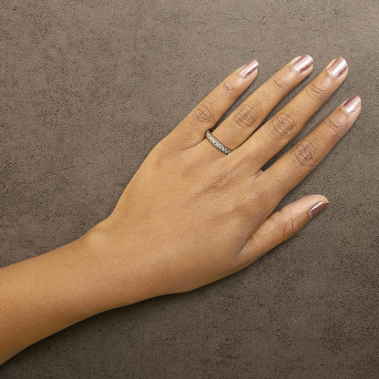 Hand with pink nails wearing a diamond ring on ring finger against a textured gray background.