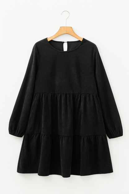 Black, long-sleeved, tiered dress on a wooden hanger against a white background.