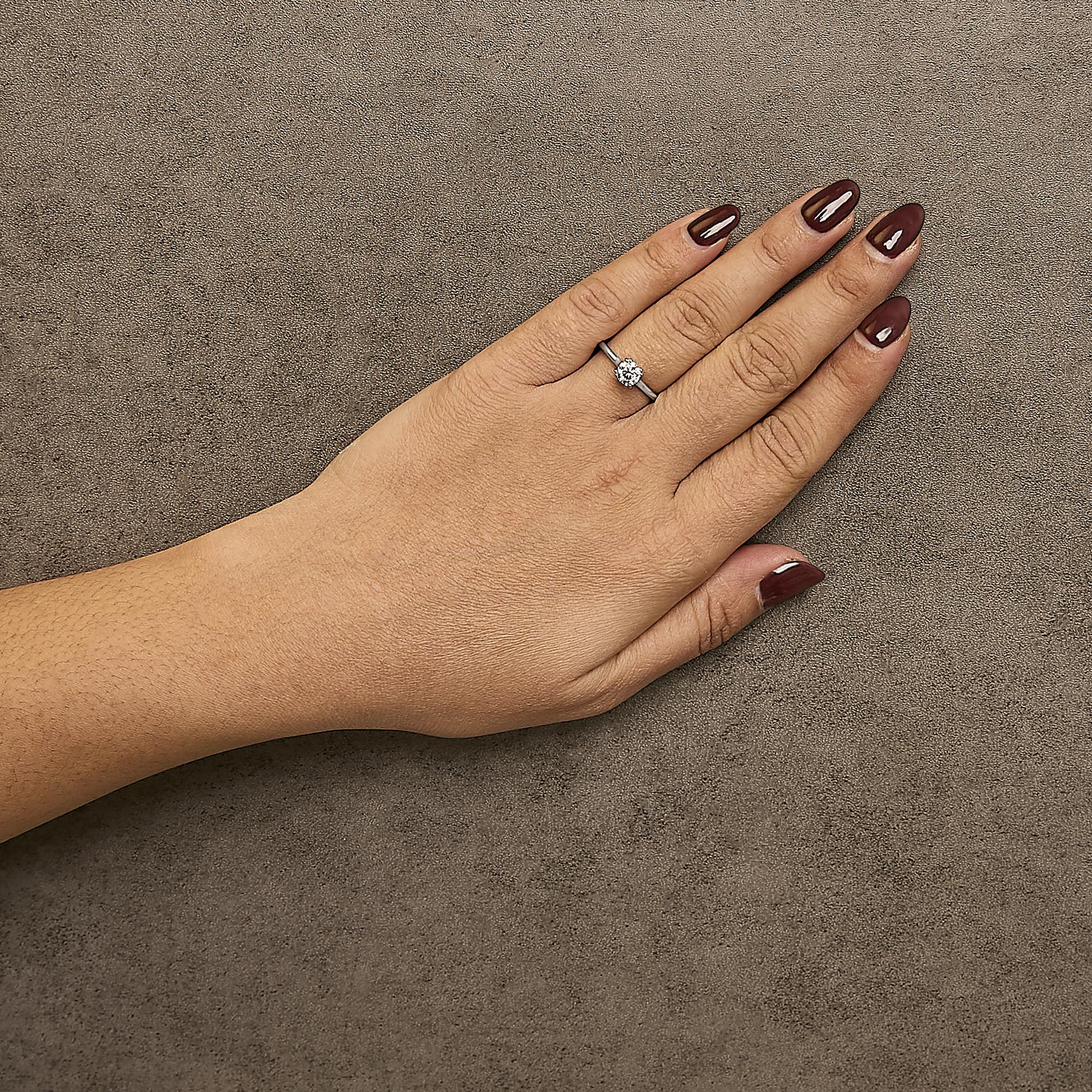 Hand with maroon nails, wearing a diamond ring, on a textured brown surface.
