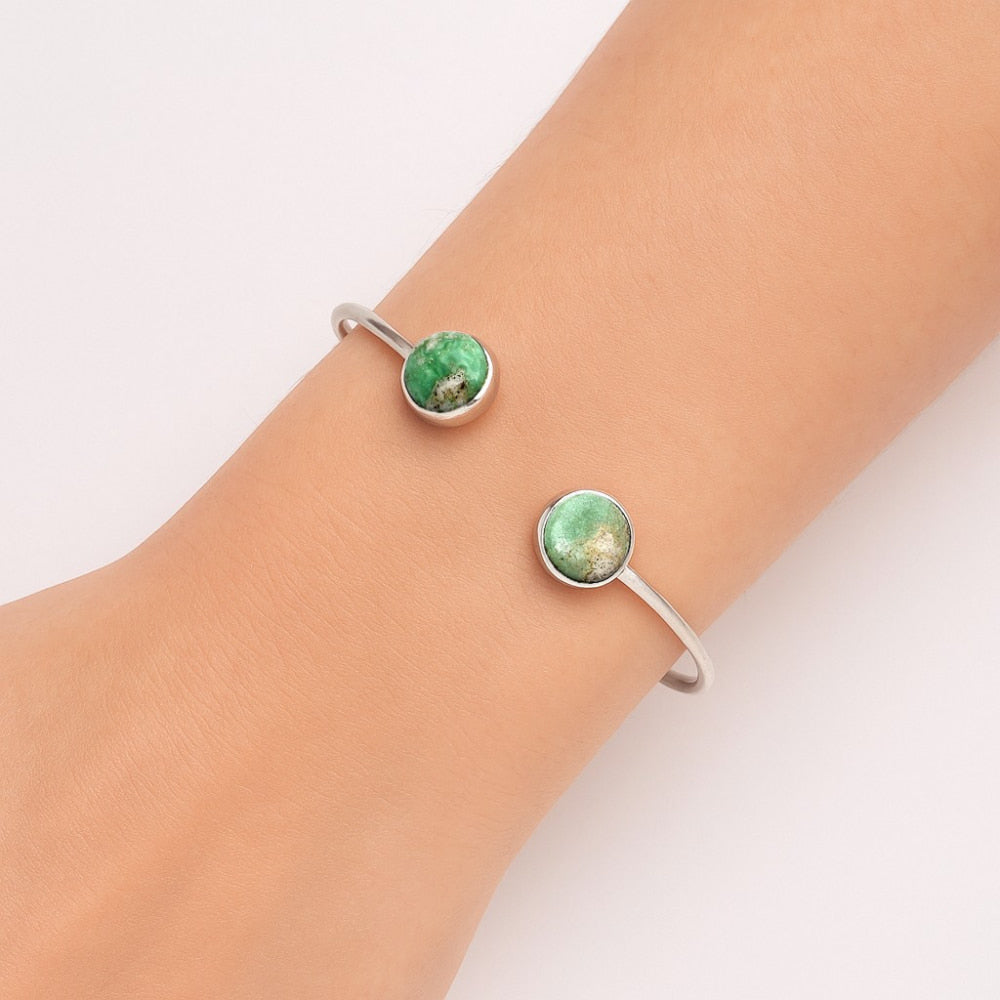Silver bracelet with two green stone accents worn on a wrist with light skin.