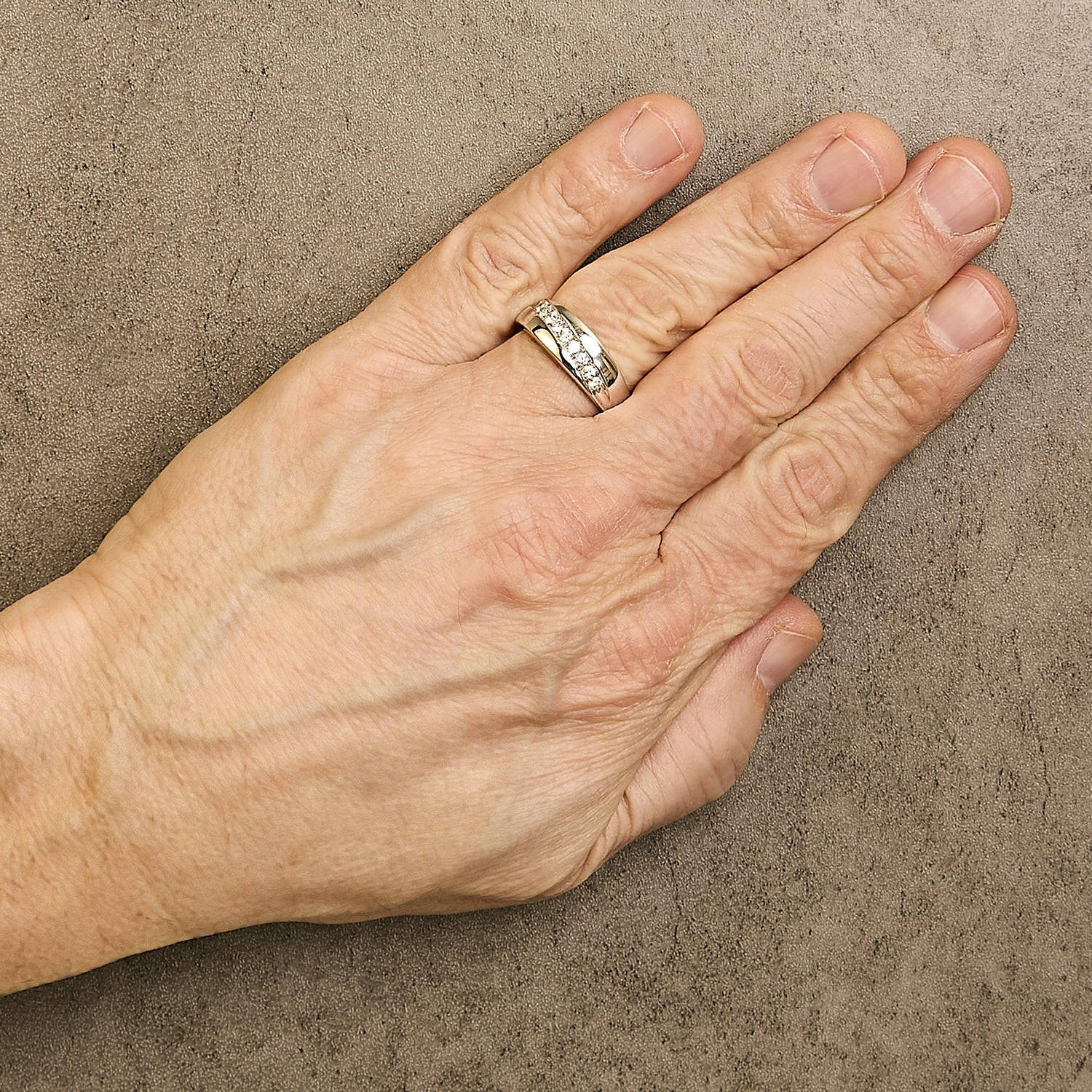Hand with a silver ring on the ring finger, resting on a textured brown surface.