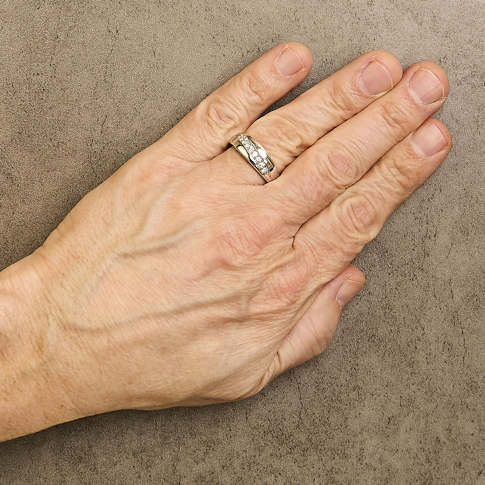 Hand with a silver ring on the ring finger, resting on a textured brown surface.