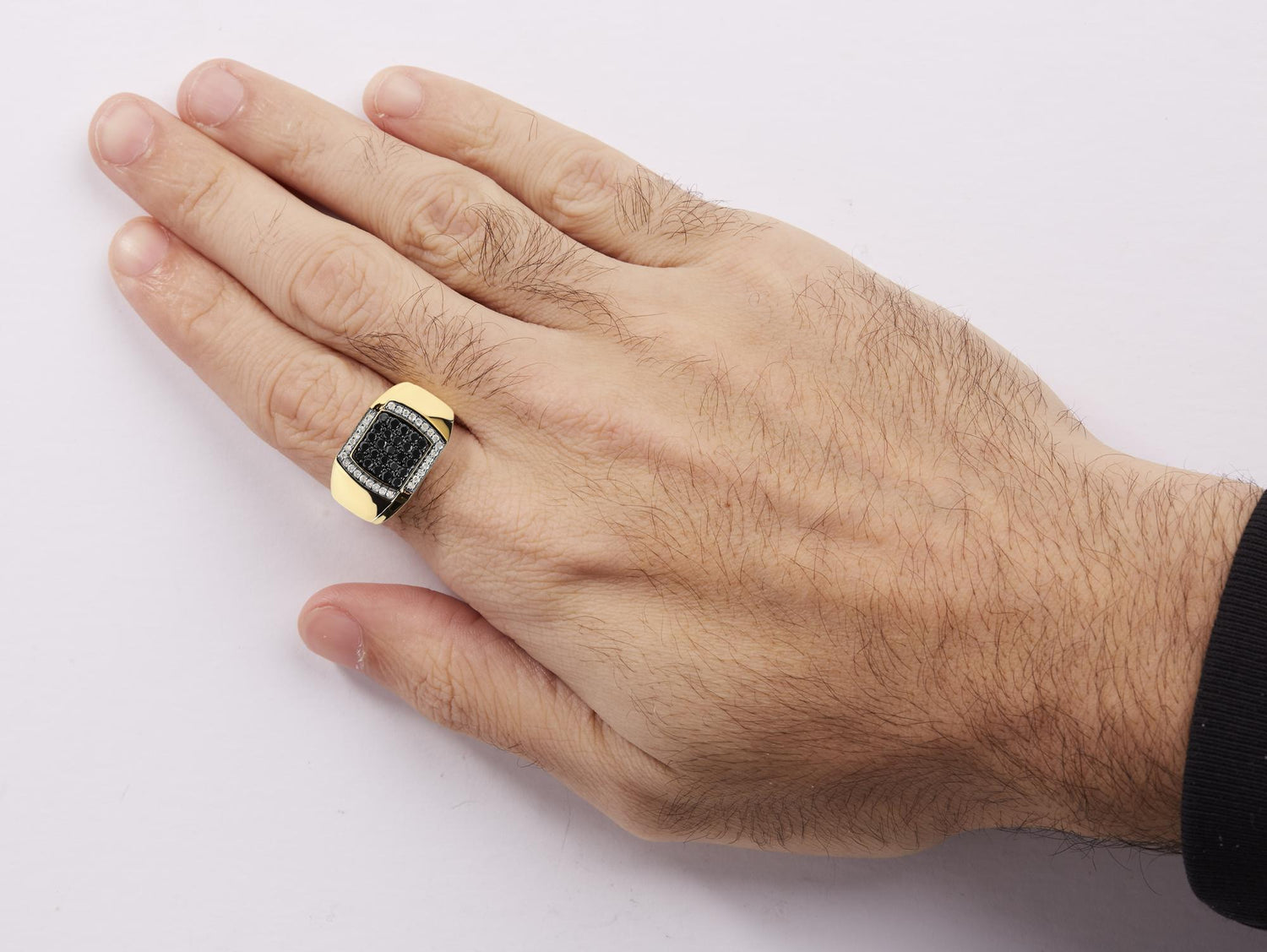 Hand with a gold ring featuring a rectangular black stone and small surrounding diamonds.