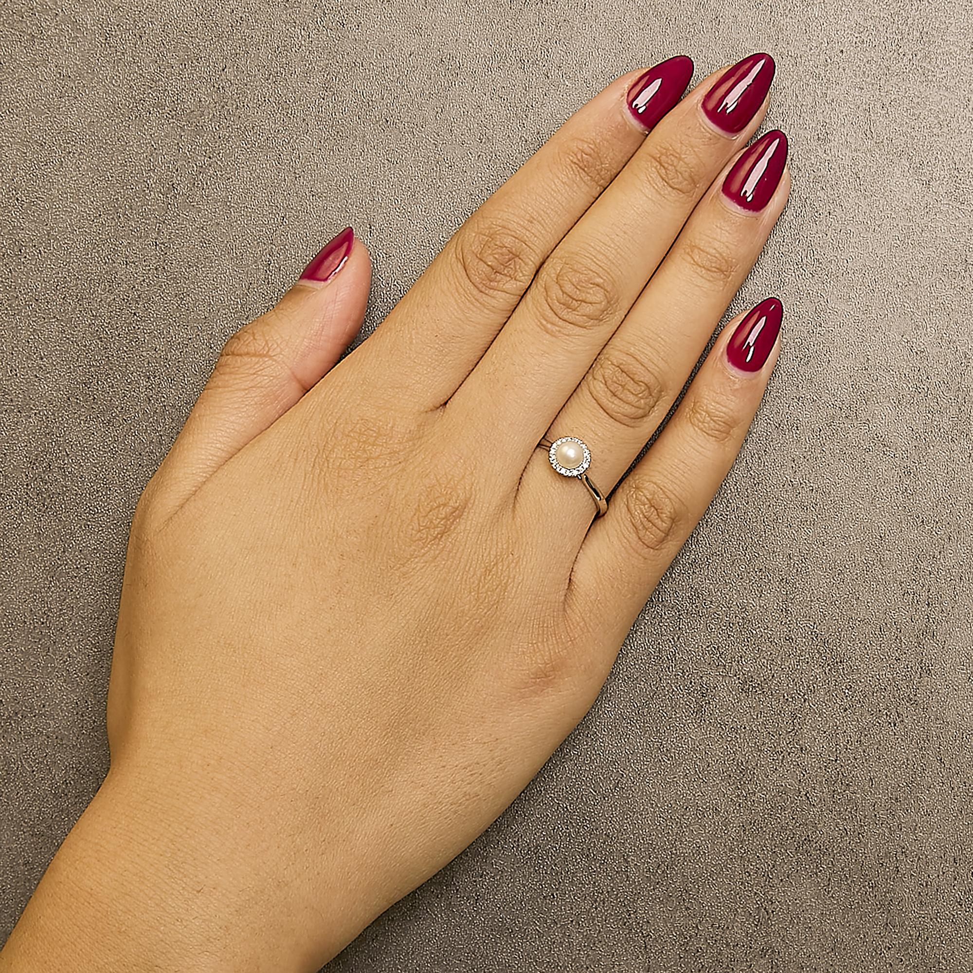 A hand with maroon nails and a pearl ring on a textured gray background.