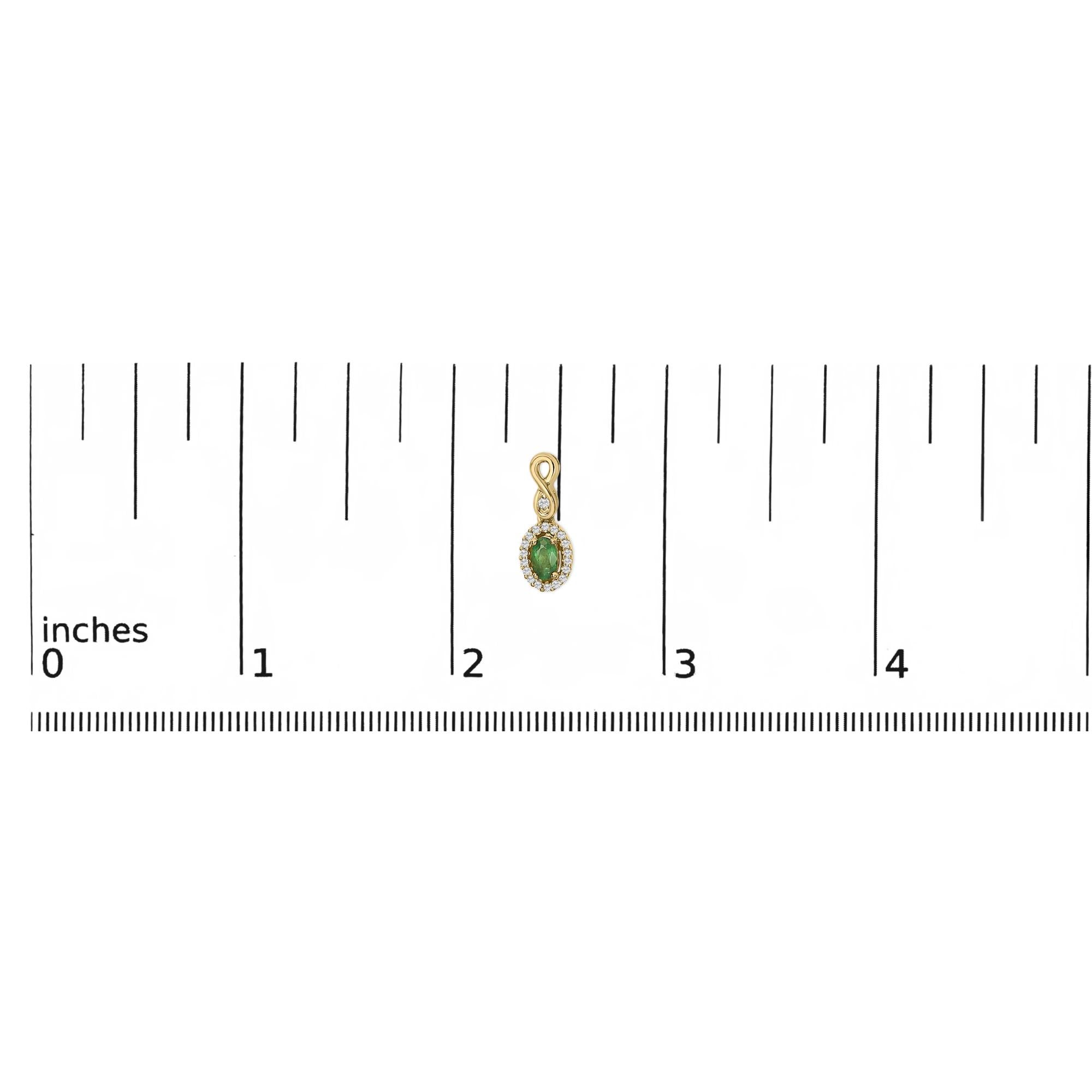 Small gold pendant with green gem, surrounded by clear stones, next to a ruler showing about 2 inches.