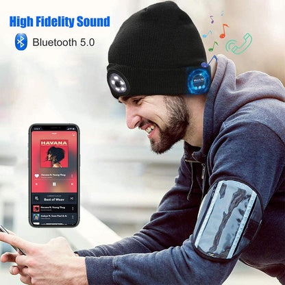 Man in a black beanie with integrated Bluetooth headphones, smartphone displaying music app.
