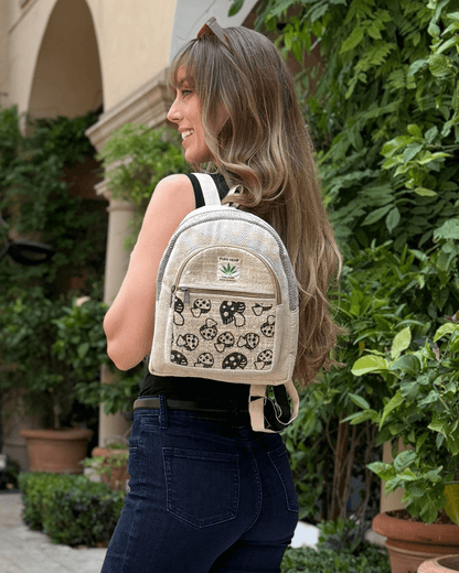 Woman with long hair wearing a black top, jeans, and a patterned beige backpack, standing outside.