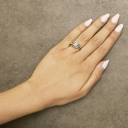 Hand with light pink nails and diamond ring on a gold band, on a textured gray surface.