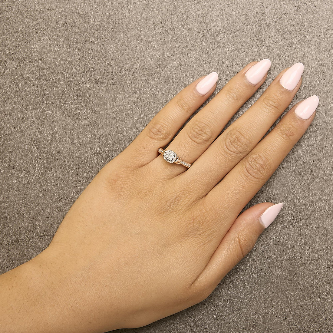 Hand with pale pink nails wearing a diamond ring on a textured gray background.