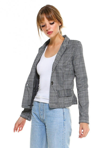 Woman in a gray plaid blazer, white tank top, and light blue jeans, standing against a white background.