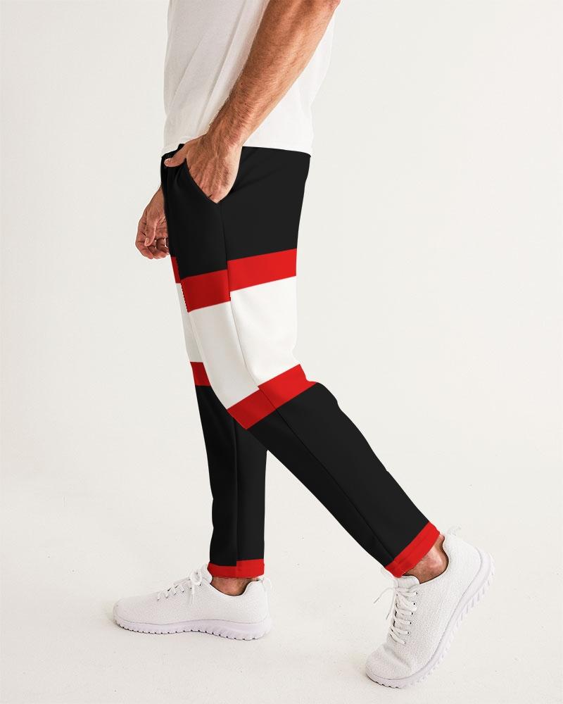 Man in color-blocked black, red, and white pants, white shirt, and white sneakers, hand in pocket.