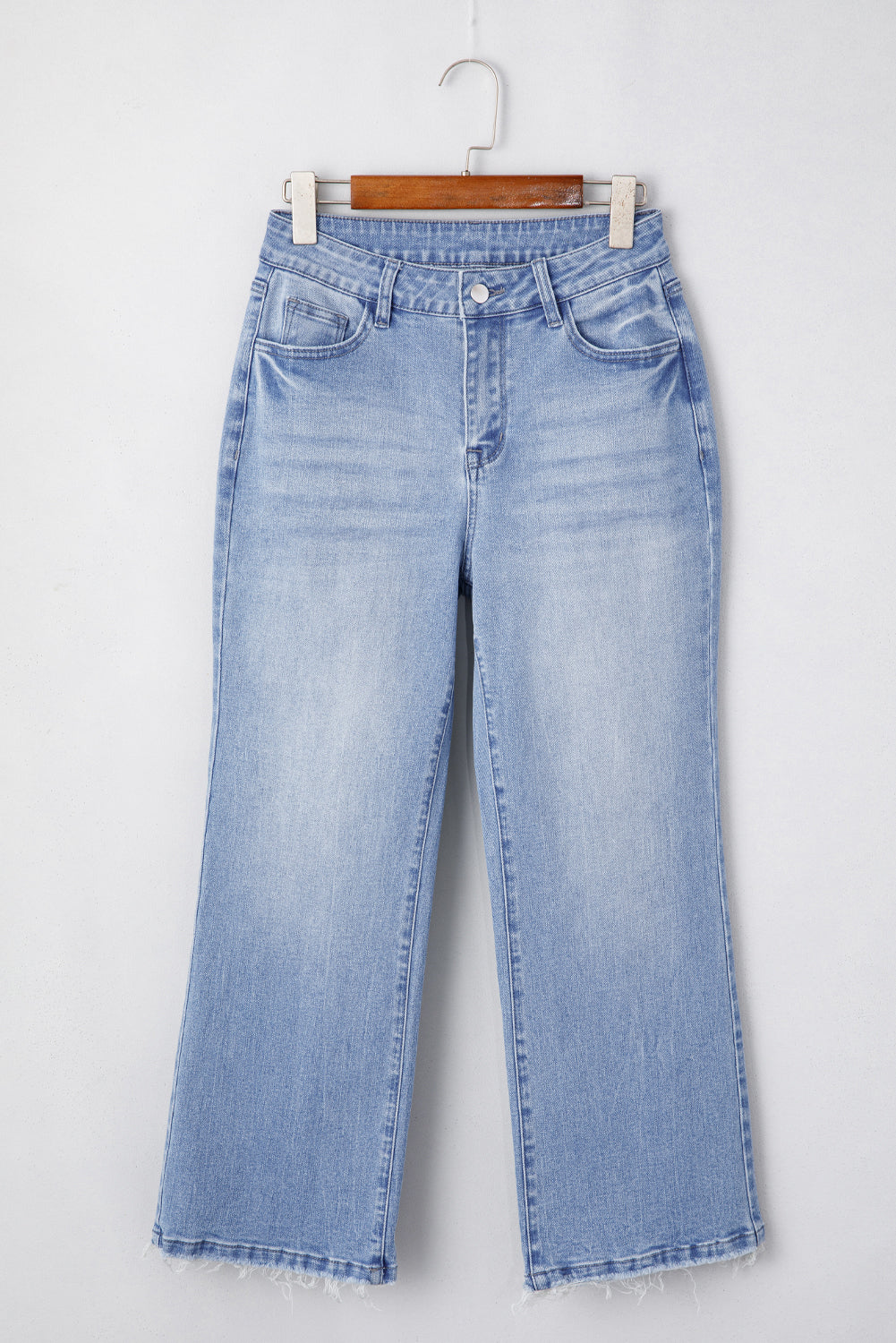Light blue flared jeans with a frayed hem, hanging on a wooden hanger.