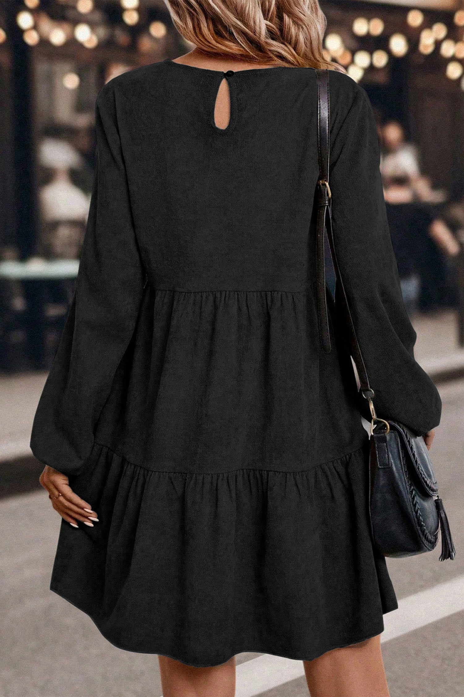Woman in a black, long-sleeved dress, with loose waves, holding a black shoulder bag.