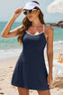 Woman in a navy beach dress, white visor, and sunglasses, standing on a sunny beach.