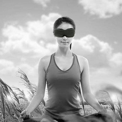 Woman meditating in a field, wearing a sleeveless top and eye mask, with a cloudy sky backdrop.
