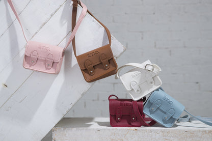 Five small leather bags in pink, brown, white, red, and blue on a white wooden surface.