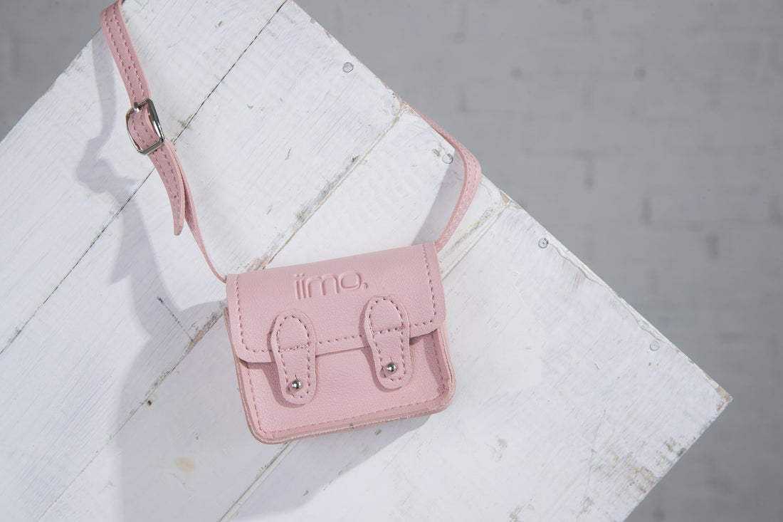Small pink leather satchel with buckles on white wooden surface.