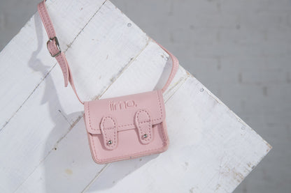 Small pink leather satchel with buckles on white wooden surface.