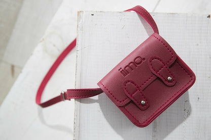 Small pink belt bag with two snap buttons, embossed logo, and an adjustable strap on white wood.