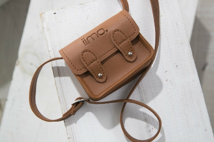 Small brown leather satchel with double buckles and a strap, on a white wooden surface.