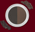 A two-tone brown and black eyeshadow in a white round case, with dark textured pieces nearby.