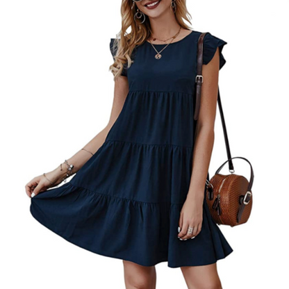 Woman in a navy tiered dress with ruffle sleeves holds a brown round bag, accessorized with jewelry.